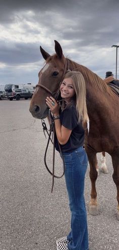 a woman standing next to a brown horse in a parking lot with other horses behind her