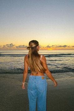 a woman standing on top of a sandy beach next to the ocean at sun set