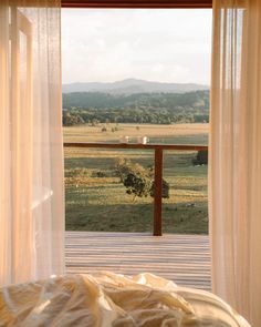 an open window with sheer curtains and a bed in the foreground, looking out onto a field