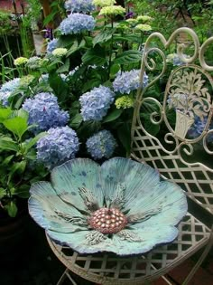 a blue flower sitting on top of a white chair next to a garden filled with flowers