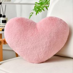 a pink heart shaped pillow sitting on top of a white couch next to a plant