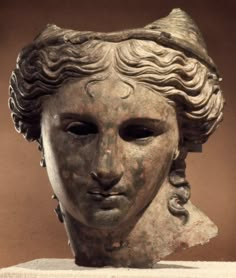 an ancient statue with wavy hair and a hat on top of it's head