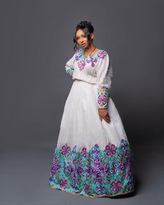 This Habesha Kemis is a true masterpiece of Ethiopian fashion, crafted with the finest Menen fabric and adorned with a stunning Tilf pattern that is sure to turn heads. The intricate details of the pattern, including the vibrant purple and blue colors and delicate shapes, are expertly woven into the fabric, creating a stunning visual effect that is both bold and regal. The dress itself is a Shimena style, designed to be form-fitting and flattering to the wearer's figure. The dress hugs the curve Bohemian Long Dress For Festivals, Bohemian Long Skirt Dress For Festivals, Festive Long Dress With Floral Embroidery, Traditional Multicolor Long Sleeve Gown, Traditional Set With Long Skirt And Floral Embroidery, Traditional Long Sleeve Multicolor Gown, Traditional Set With Floral Embroidery And Long Skirt, Traditional Sets With Floral Embroidery And Long Skirt, Multicolor Long Sleeve Dresses For Traditional Ceremonies