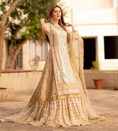 a woman in a white and gold lehenga standing on the ground with her hands on her hips