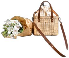 a wicker bag with flowers in it next to a brown leather handbag on a white background