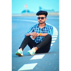 a man sitting on the side of a road with his legs crossed and wearing sunglasses