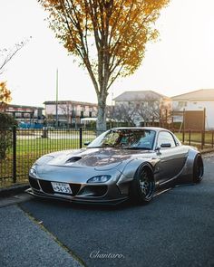 a silver sports car parked on the street next to a fence and tree in front of it