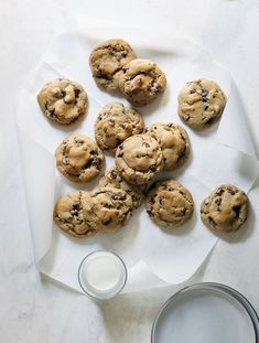 chocolate chip cookies and a glass of milk on a white tablecloth with parchment paper