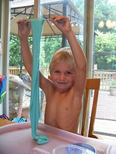 a young boy sitting at a table with his arms in the air holding up a blue object