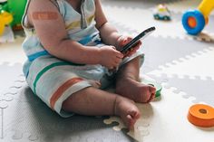 a baby sitting on the floor playing with a cell phone by jovo studio for stocks & bond