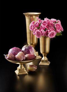 three gold vases with pink flowers and onions in them on a black table top