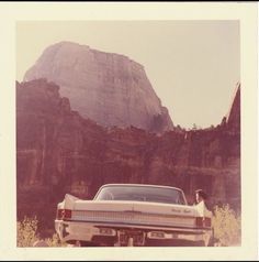 an old photo of a car parked in front of a large rock formation with a dog standing on the hood