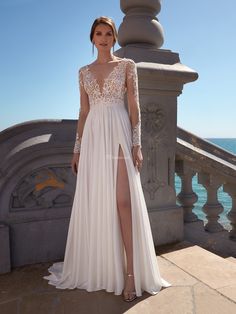 a woman in a white dress standing on a balcony next to the ocean with her legs crossed