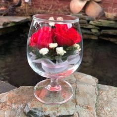 a clear glass with some red and white flowers in it sitting on top of a rock