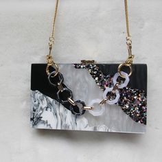 Editor's Notes: A delicate combination of tones. A rectangular clutch with a geometrical pattern. The surface has a raw water-like texture and a resin-like look. This clutch is sure to grab attention. There is enough room for all your essentials. The clutch comes with two chains: a short one to carry the clutch as a handbag and a long one to carry the clutch on the shoulder. Size 7 x 4.3 x 2 inches (18 x 11 x 5 cm) Material PVC, polyester, and acrylic Details Removable chain shoulder strap Clasp Square Clutch With Chain Strap As Gift, Trendy Square Clutch For Evening, Rectangular Clutch With Chain For Gift, Modern Rectangular Clutch For Party, Modern Rectangular Party Clutch, Trendy Clutch With Chain Strap For Gift, Chic Square Clutch For Gift, Trendy Clutch With Chain Strap As A Gift, Trendy Rectangular Evening Clutch