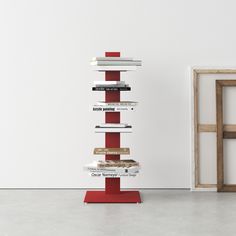 a stack of books sitting on top of a red stand in front of a white wall