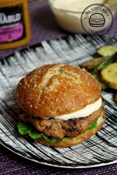 a hamburger with lettuce, cheese and pickles on a plate next to some mayonnaise