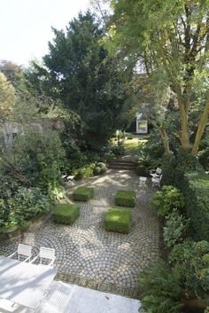 a stone path in the middle of a garden with white chairs and bushes on either side