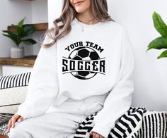 a woman sitting on a couch wearing a sweatshirt that says your team sogger