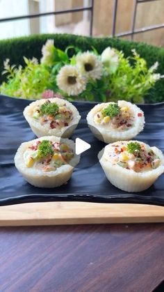 small food items are placed on a black plate with flowers in the background and a wooden tray holding broccoli