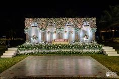 a decorated stage with flowers and greenery on the side at night in front of a building