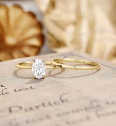 two engagement rings sitting on top of an old book with writing in the back ground