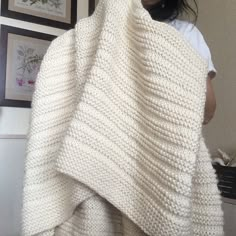 a woman holding up a white knitted blanket