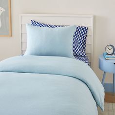 a bed with blue sheets and pillows on top of it next to a small table