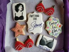 some decorated cookies are in a box with purple tissue paper on the bottom and one has an image of a woman's bra