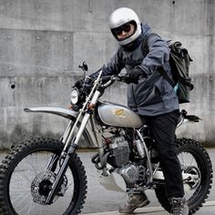 a man riding on the back of a silver motorcycle down a street next to a cement wall