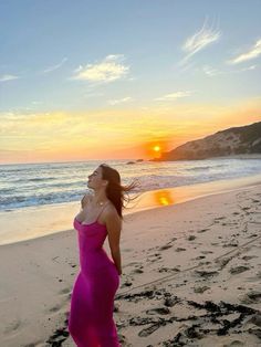 a woman standing on top of a sandy beach next to the ocean in a pink dress