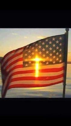 an american flag with a cross on it flying in the air over water at sunset