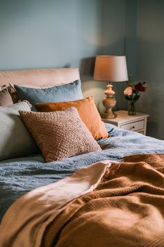 a bed with pillows and blankets on top of it next to a night stand in front of a blue wall