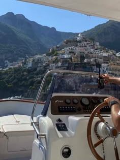 a man driving a boat in front of a city on top of a mountain range