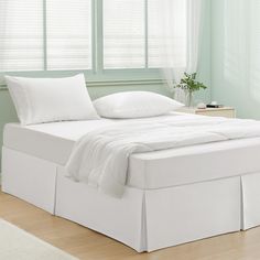 a bed with white sheets and pillows on top of it next to a wooden floor