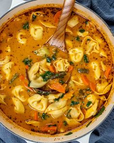 a pot filled with tortellini soup on top of a blue towel and wooden spoon