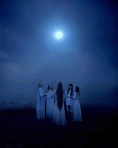 three women dressed in white standing on a hill at night with the moon behind them