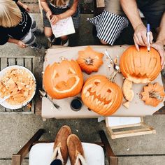 people are carving pumpkins with carved faces on them and sitting at a table outside