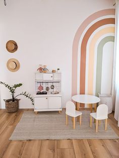 a white table and chairs in a room with rainbow painted on the wall behind it