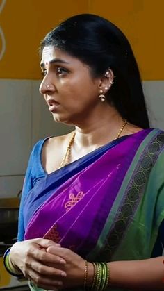 a woman wearing a purple and green sari with her hands folded in front of her chest