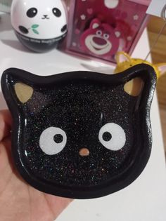 a hand holding up a black cat shaped brooch with glitter on it's face