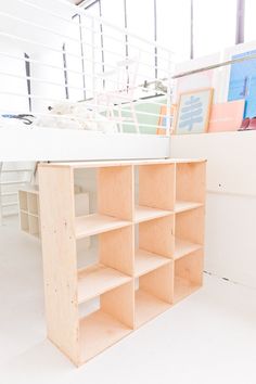 a white loft bed with shelving unit in the foreground and bookshelves on the other side