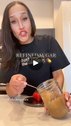 a woman holding a spoon in front of a jar filled with liquid and strawberries