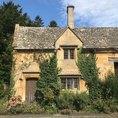 an old stone house with ivy growing on it's roof and windows, surrounded by greenery