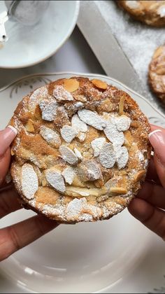 a person holding up a pastry with white powdered sugar on top and almonds in the middle