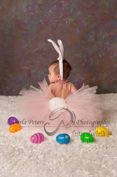 a baby wearing a pink tutu and bunny ears sitting on top of a white rug