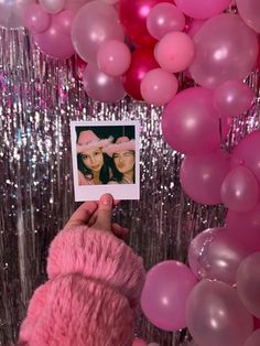 a person holding up a polaroid photo in front of pink and silver foil balloons