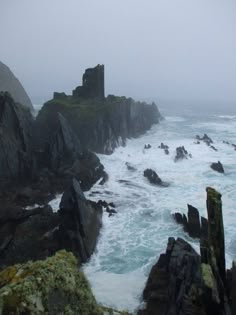 the ocean is choppy with waves coming in to shore and an old castle on top