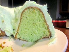 a white plate topped with a cake covered in green frosting next to a slice of cake