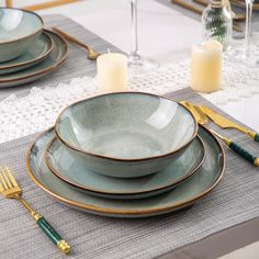 a place setting with plates and silverware on a gray table cloth, gold trimming